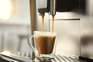 Espresso machine pouring coffee into glass cup against blurred background, closeup