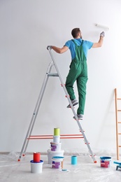 Male decorator painting wall with roller indoors