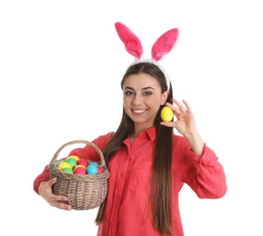 Beautiful woman in bunny ears headband holding basket with Easter eggs on white background