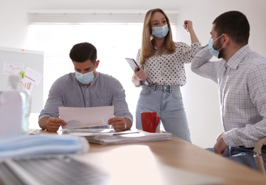 Photo of Coworkers with protective masks making elbow bump in office. Informal greeting during COVID-19 pandemic