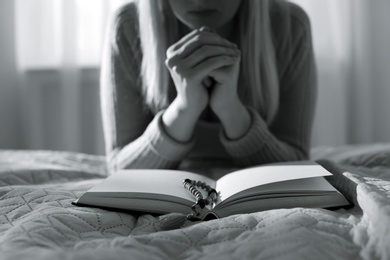 Religious young woman praying over Bible in bedroom. Black and white effect