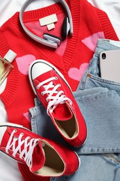 Pair of stylish red shoes, clothes and smartphone on white fabric, flat lay