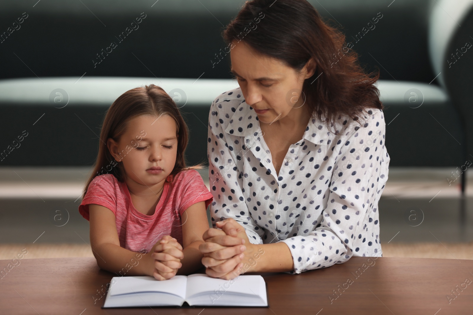 Photo of Mature woman with her little granddaughter praying together over Bible at home