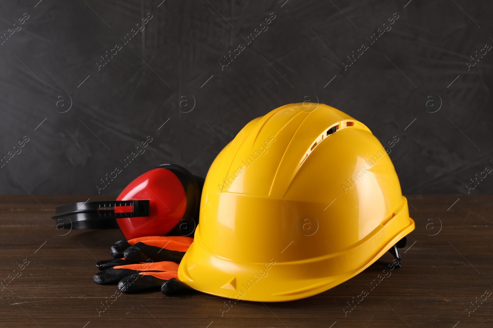 Photo of Hard hat, earmuffs and gloves on wooden table. Safety equipment