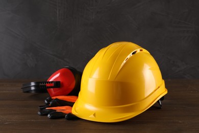 Hard hat, earmuffs and gloves on wooden table. Safety equipment