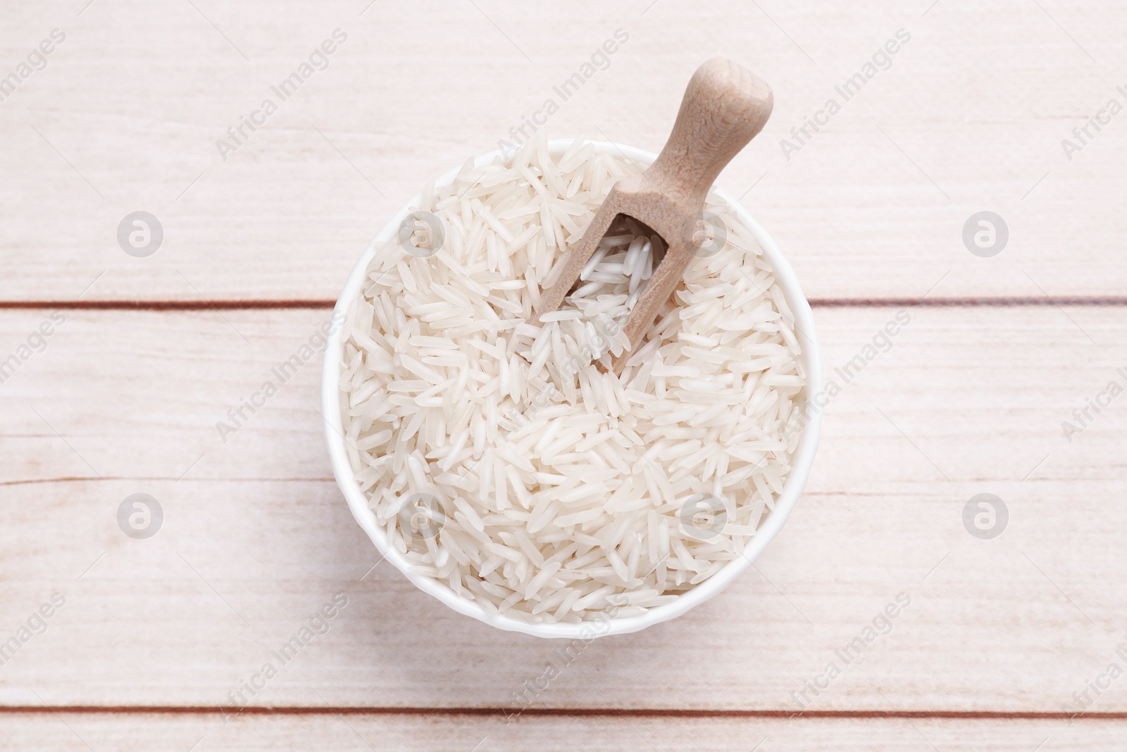 Photo of Raw basmati rice and scoop in bowl on white wooden table, top view