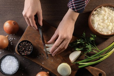 Photo of Woman cutting ripe onion at wooden table, top view