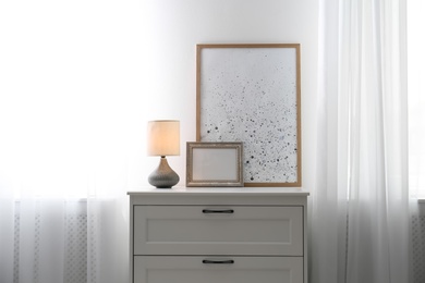 Photo of Modern chest of drawers with lamp near window in room