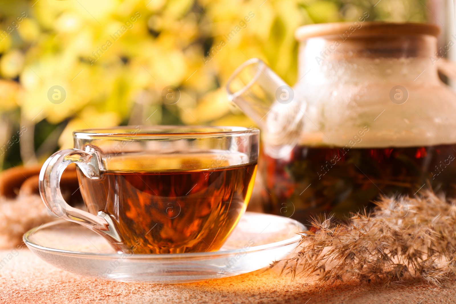 Photo of Hot tea and beautiful dry reed on beige textured table outdoors, closeup. Autumn atmosphere