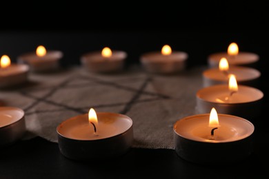 Photo of Fabric with star of David and burning candles on black background, closeup. Holocaust memory day
