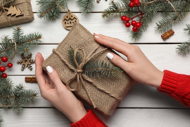 Photo of Woman with Christmas gift at white wooden table, top view