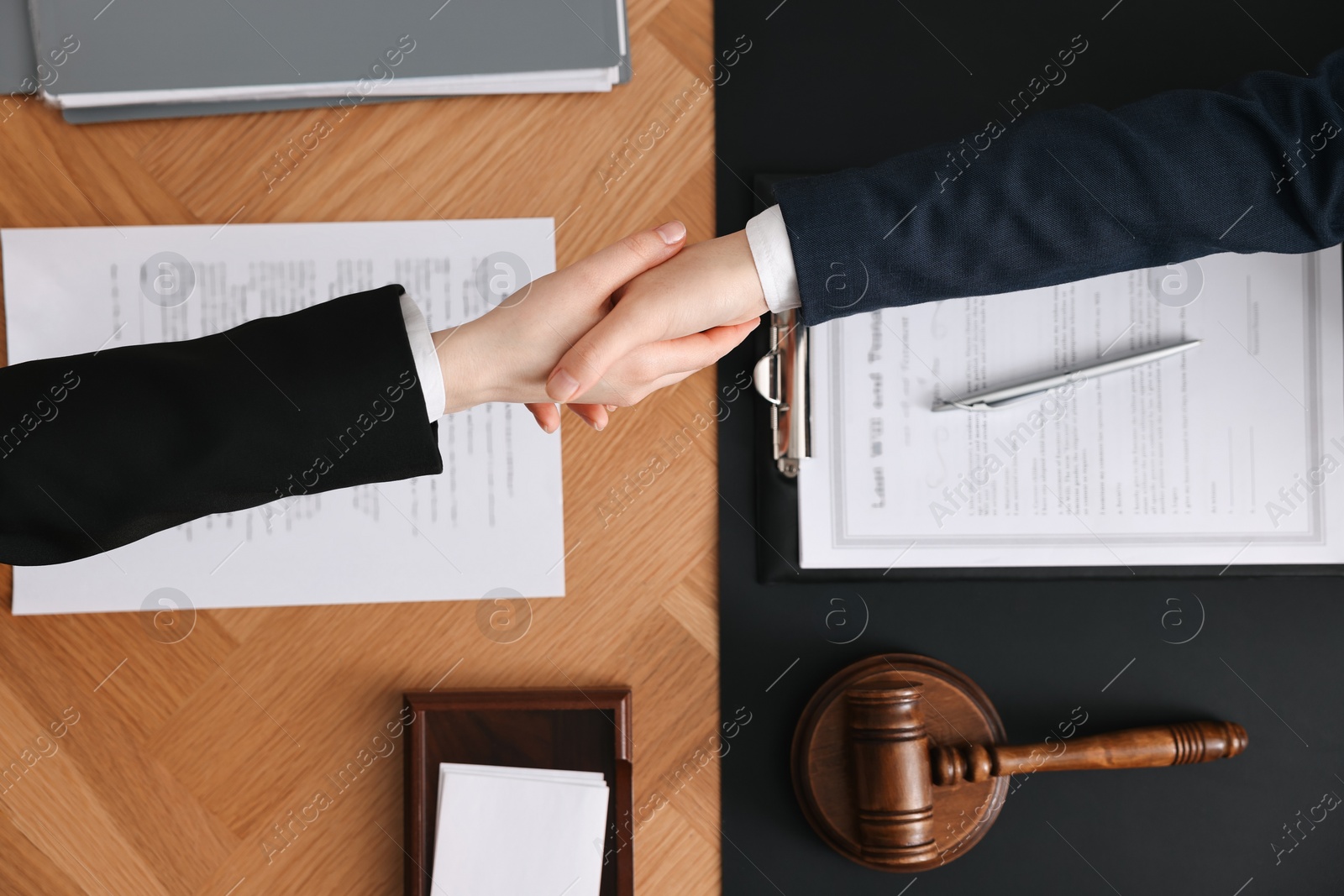 Photo of Notary shaking hands with client at wooden table, top view