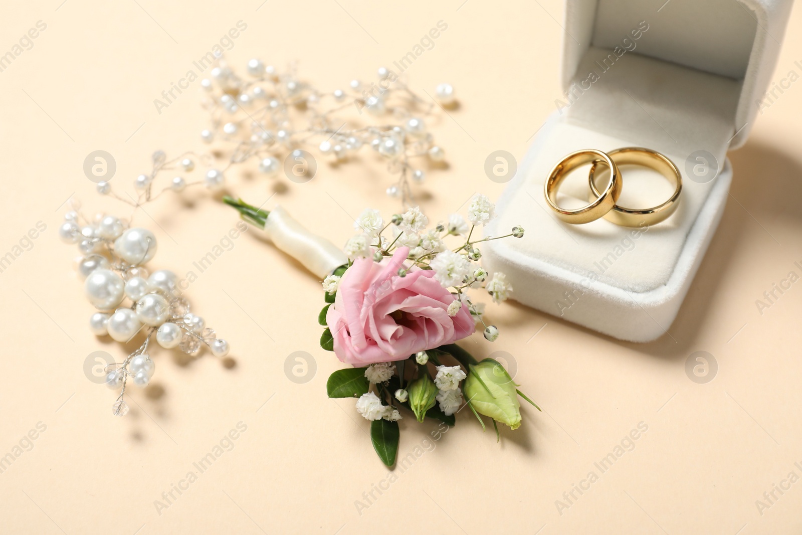 Photo of Wedding stuff. Stylish boutonniere, rings and decor on beige background, closeup