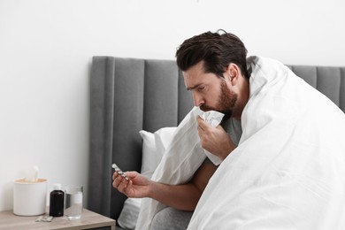 Photo of Sick man with tissue coughing on bed at home. Cold symptoms