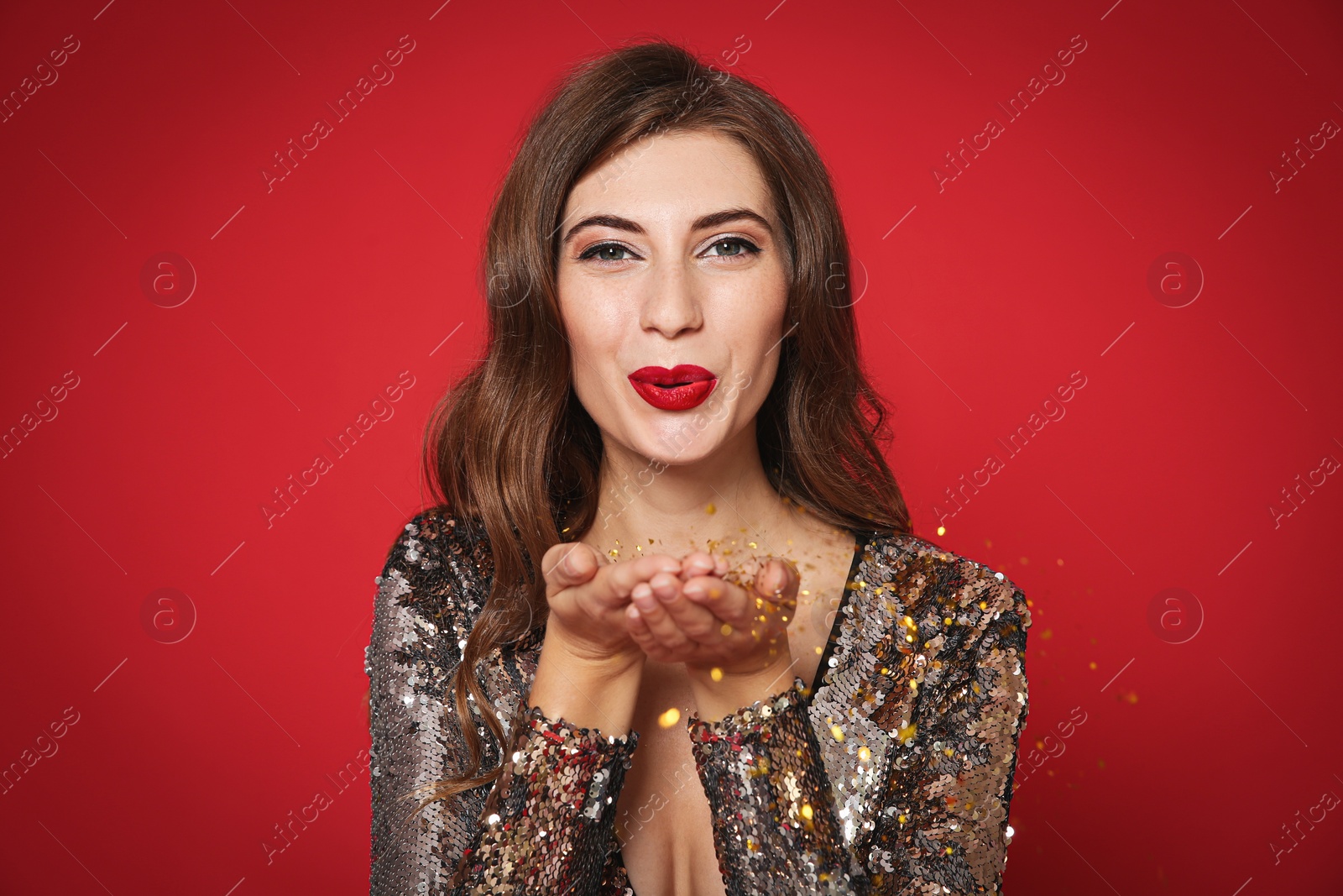 Photo of Beautiful woman blowing glitter on red background. Christmas party