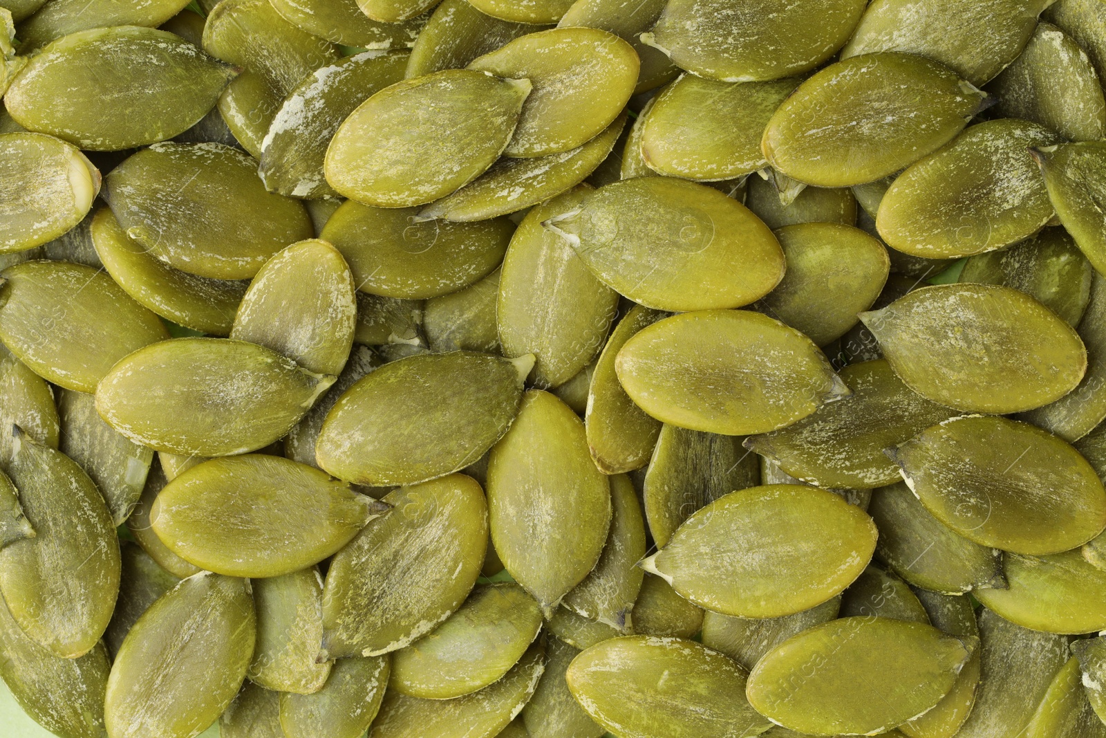 Photo of Many peeled pumpkin seeds as background, top view