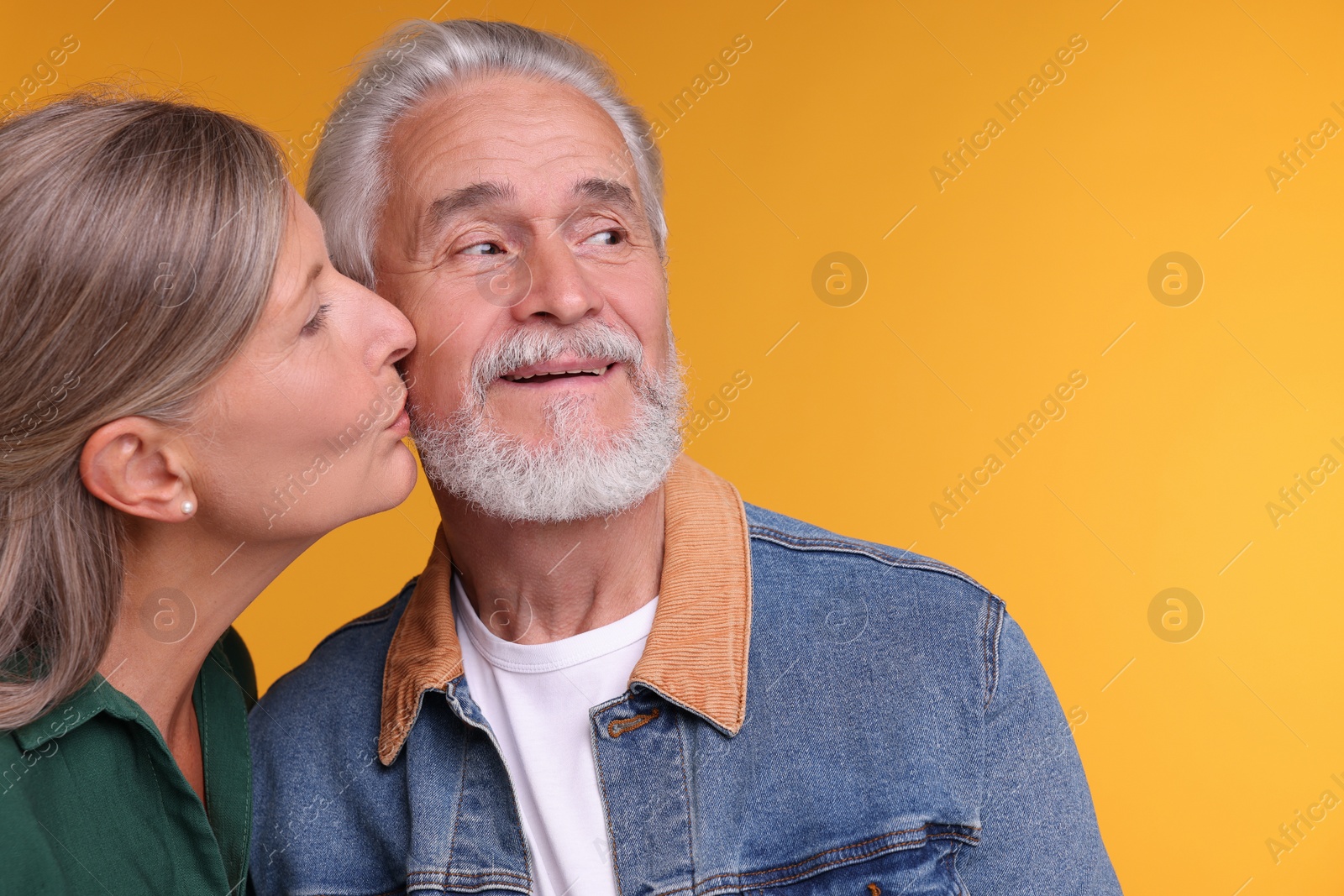 Photo of Senior woman kissing her beloved man on orange background, space for text