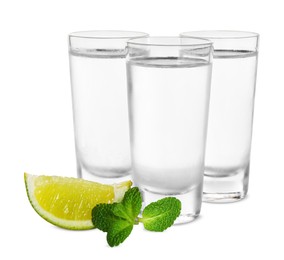 Shot glasses of vodka with lime and mint on white background