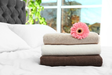 Stack of clean towels and beautiful gerbera flower on bed. Space for text