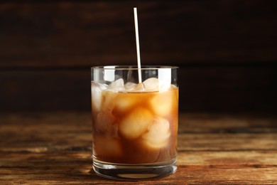 Pouring milk into glass with coffee on wooden table