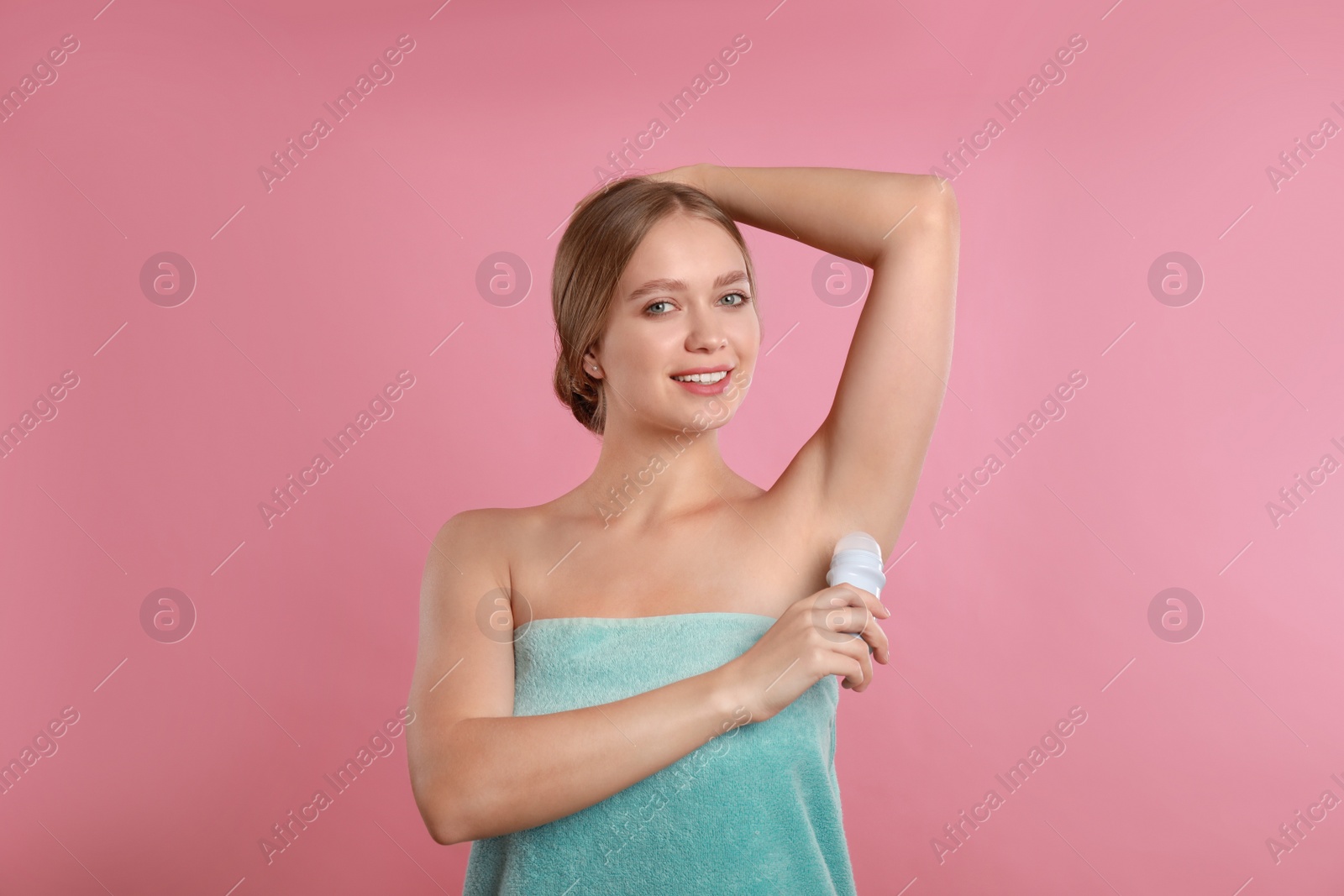 Photo of Young woman applying deodorant to armpit on pink background