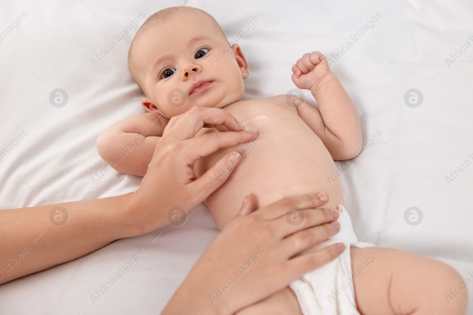 Photo of Woman applying body cream onto baby`s skin on bed, closeup