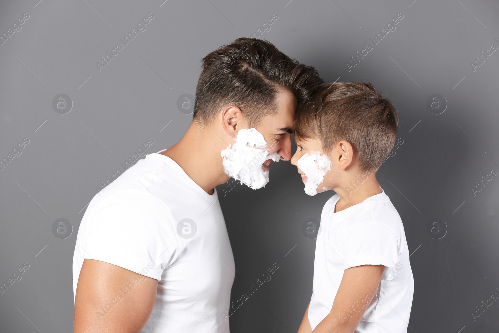 Photo of Father and son with shaving foam on faces against color background