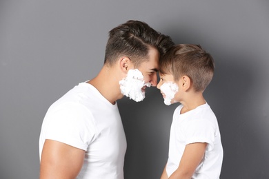 Photo of Father and son with shaving foam on faces against color background