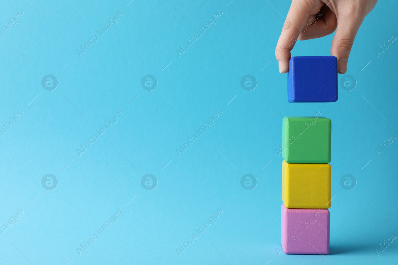 Photo of Woman stacking colorful cubes on light blue background, closeup and space for text. Management concept