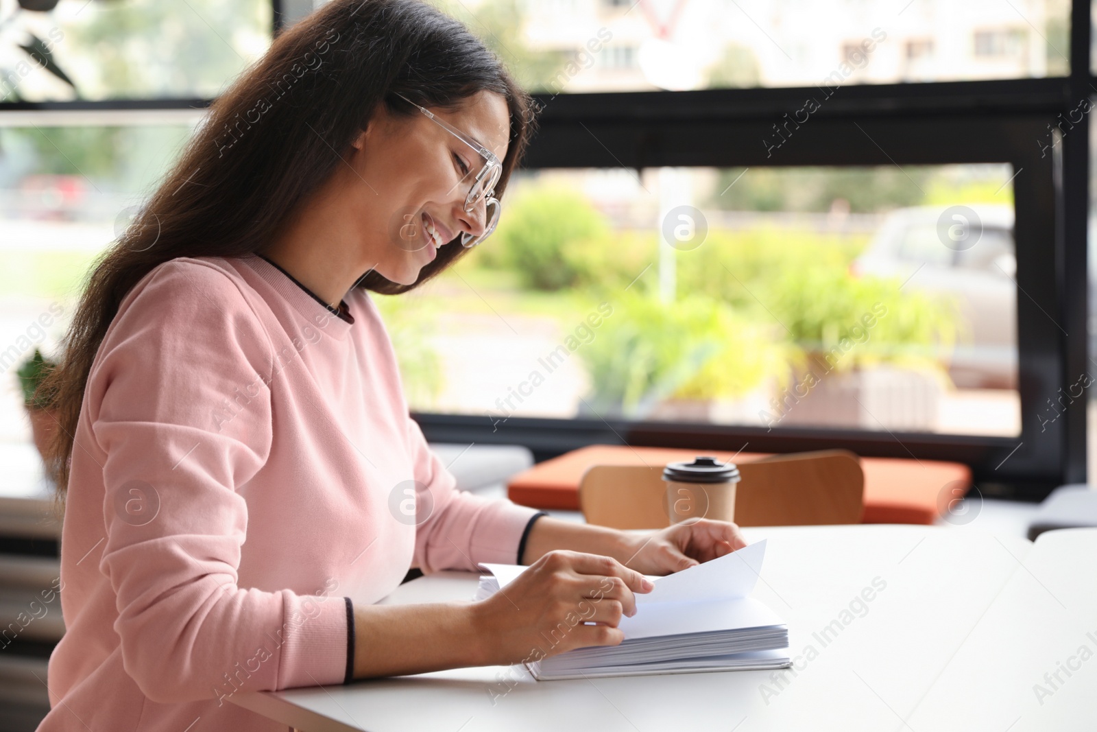 Photo of Young woman reading book at table in library. Space for text