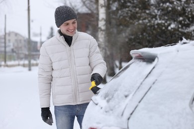 Man cleaning snow from car window outdoors