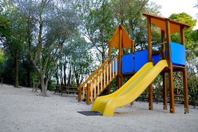 Photo of Empty playground with beautiful slide, benches and trees in park. Space for text