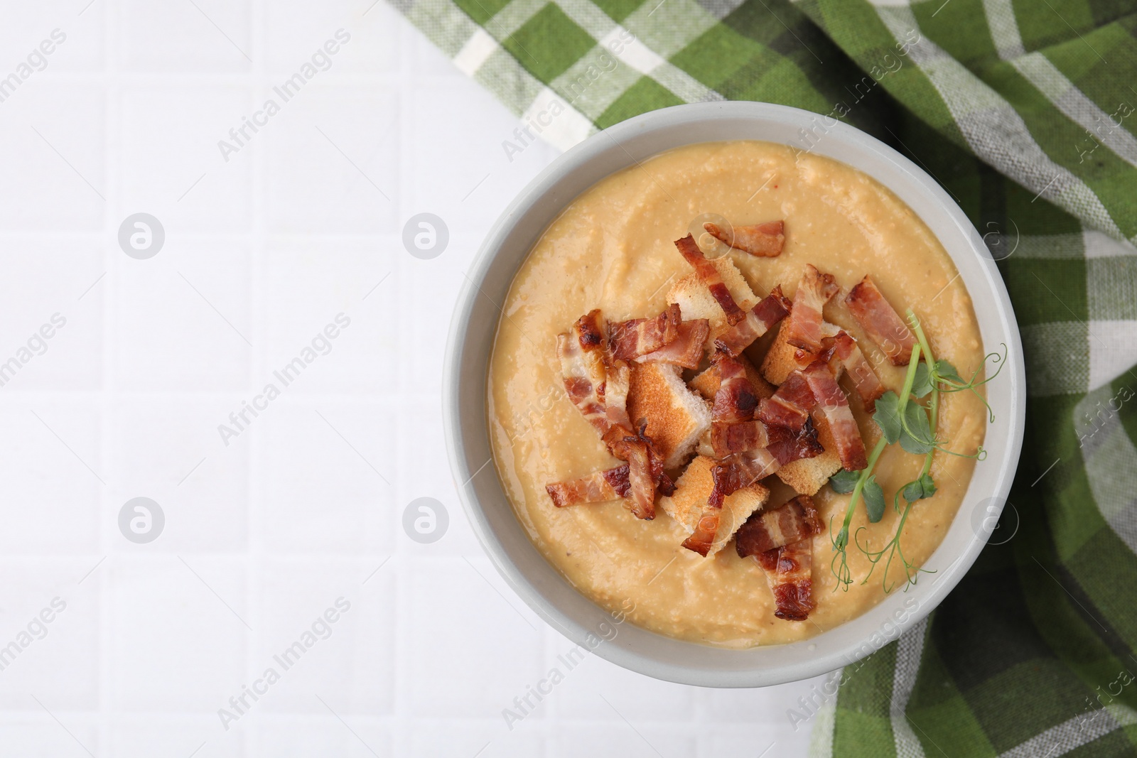 Photo of Delicious lentil soup with bacon and croutons on white tiled table, top view. Space for text