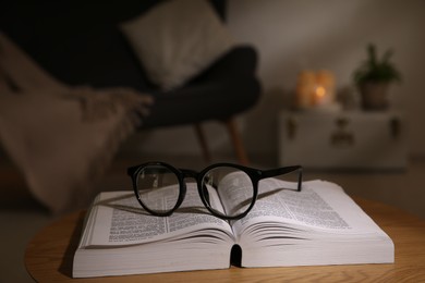 Book and glasses on wooden coffee table indoors at night
