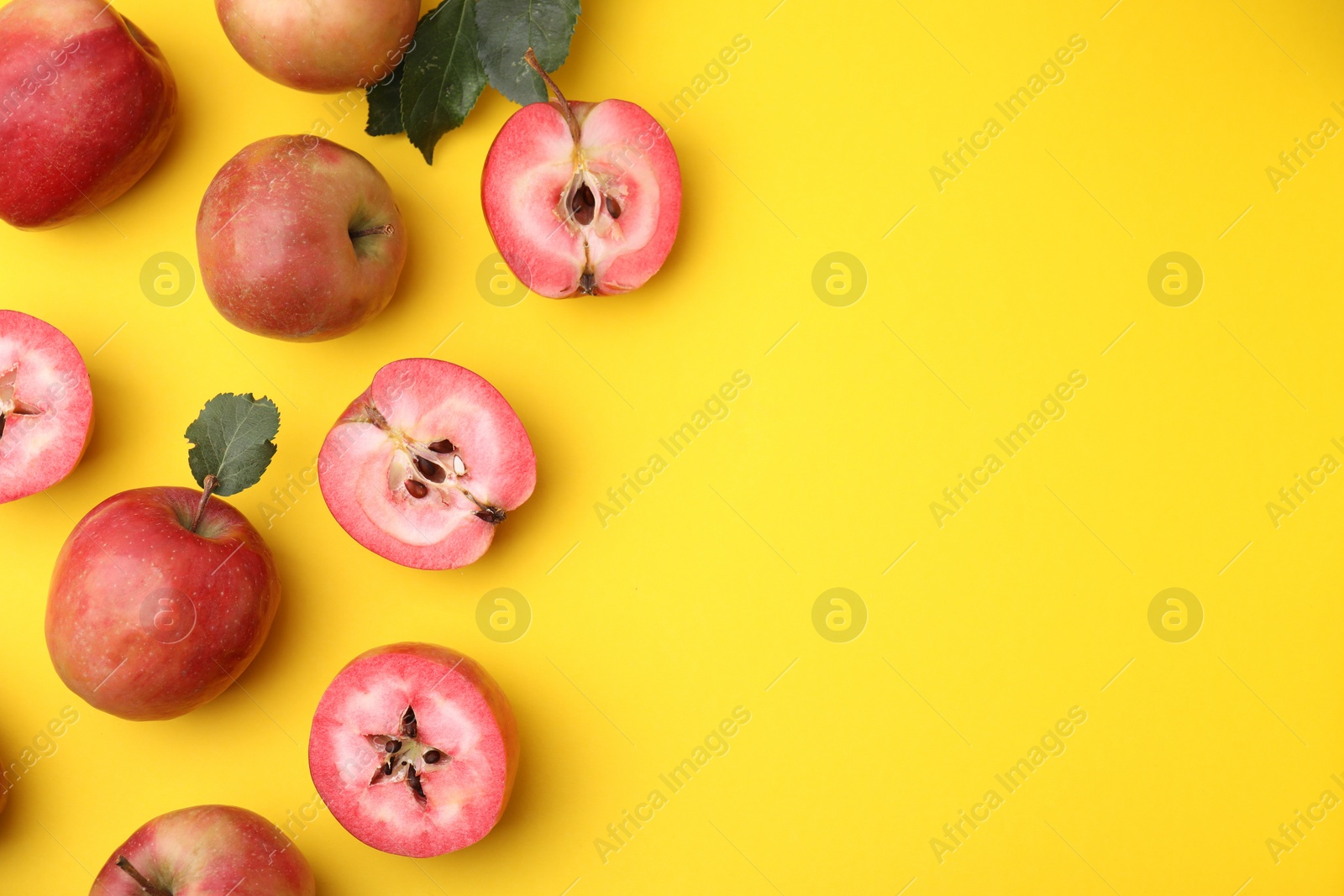 Photo of Tasty apples with red pulp and leaves on yellow background, flat lay. Space for text