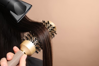 Hairdresser blow drying client's hair on beige background, closeup. Space for text