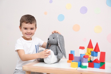 Photo of Cute child playing doctor with stuffed toy at table in hospital