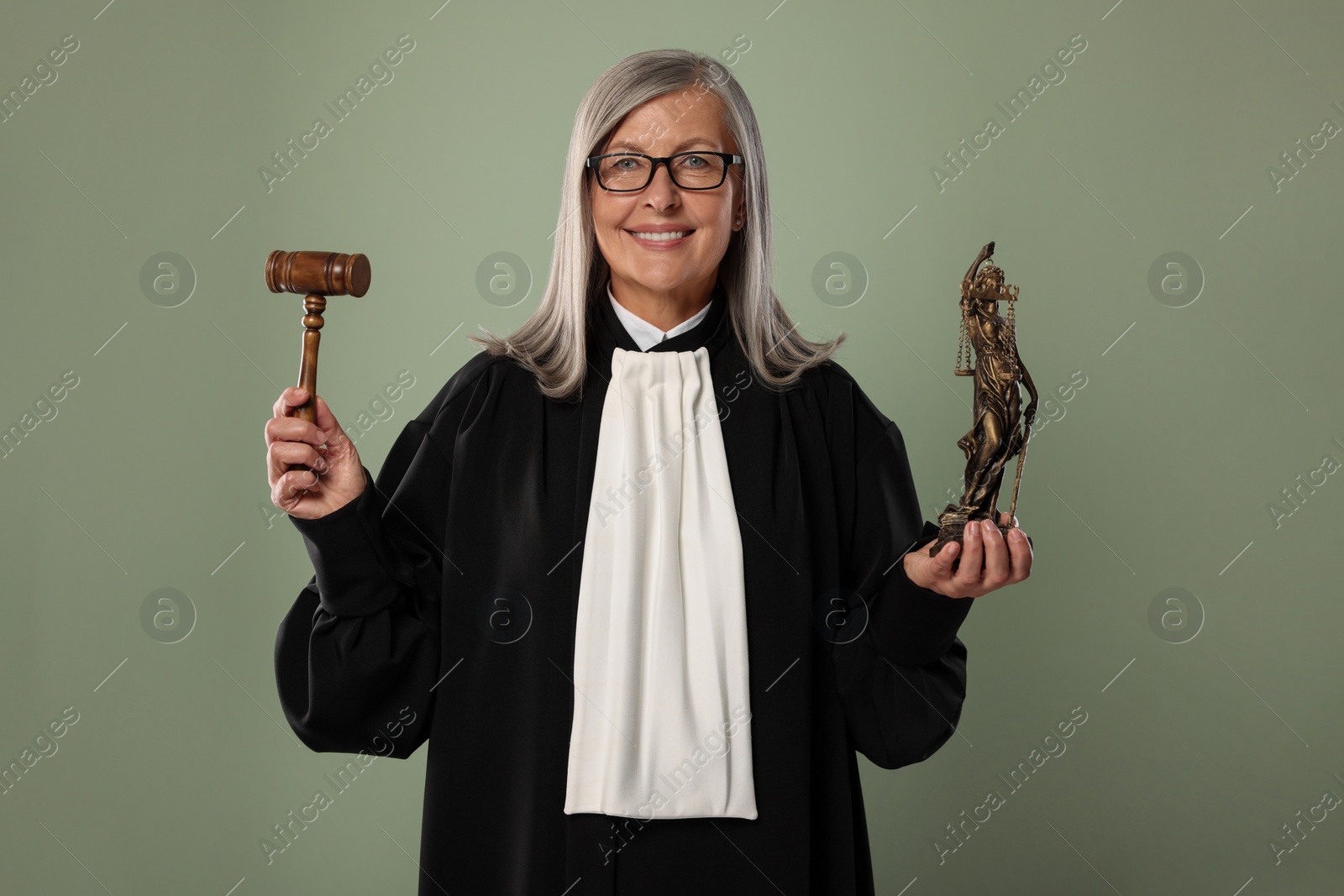 Photo of Smiling senior judge with gavel and figure of Lady Justice on green background