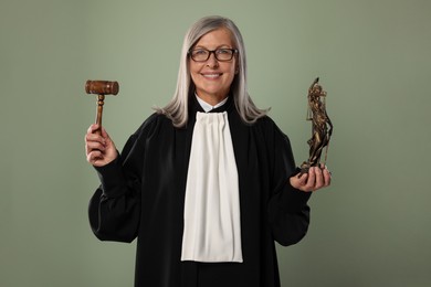 Smiling senior judge with gavel and figure of Lady Justice on green background