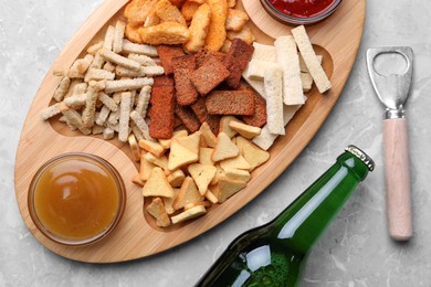 Photo of Different crispy rusks served with dip sauces and beer on light marble table, flat lay