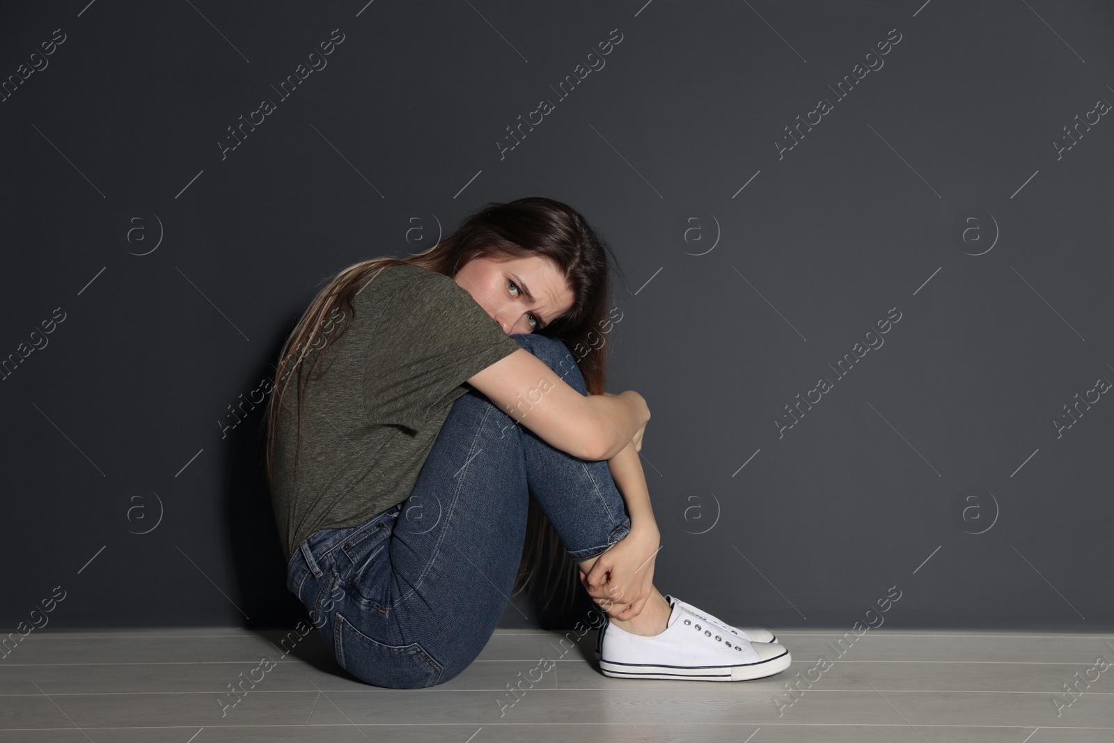 Photo of Upset young woman sitting on floor near grey wall. Space for text