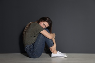 Upset young woman sitting on floor near grey wall. Space for text
