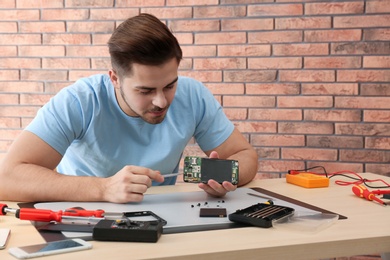 Photo of Technician repairing broken smartphone at table in workshop