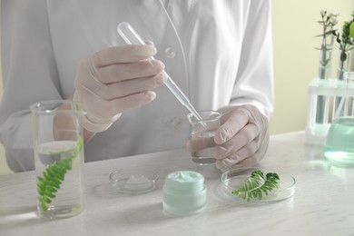 Photo of Scientist making cosmetic product at white table in laboratory, closeup
