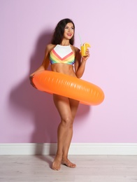 Beautiful young woman with inflatable ring and glass of cocktail near color wall