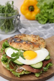 Photo of Tasty bagel with cured ham, egg, cucumber and salad mix on table