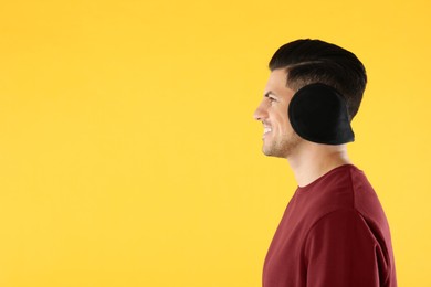 Photo of Man wearing stylish earmuffs on yellow background. Space for text