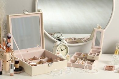 Photo of Jewelry boxes with many different accessories, perfumes, makeup brushes and alarm clock on white table