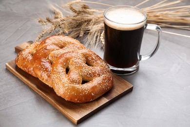 Photo of Tasty pretzels, glass of beer and wheat spikes on grey table