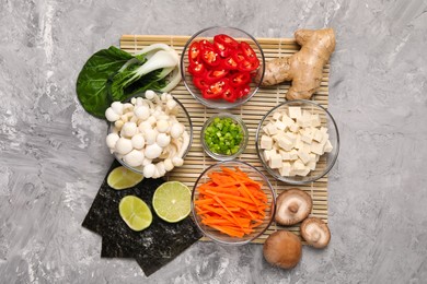 Photo of Cooking delicious ramen soup. Different ingredients on gray textured table, flat lay
